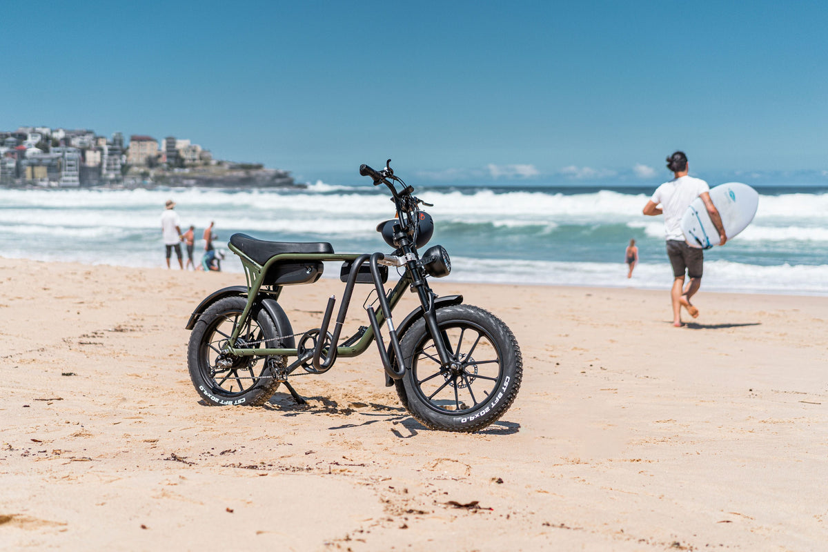 A Mamba Sahara parked on Bondi Beach while a surfer heads into the waves.